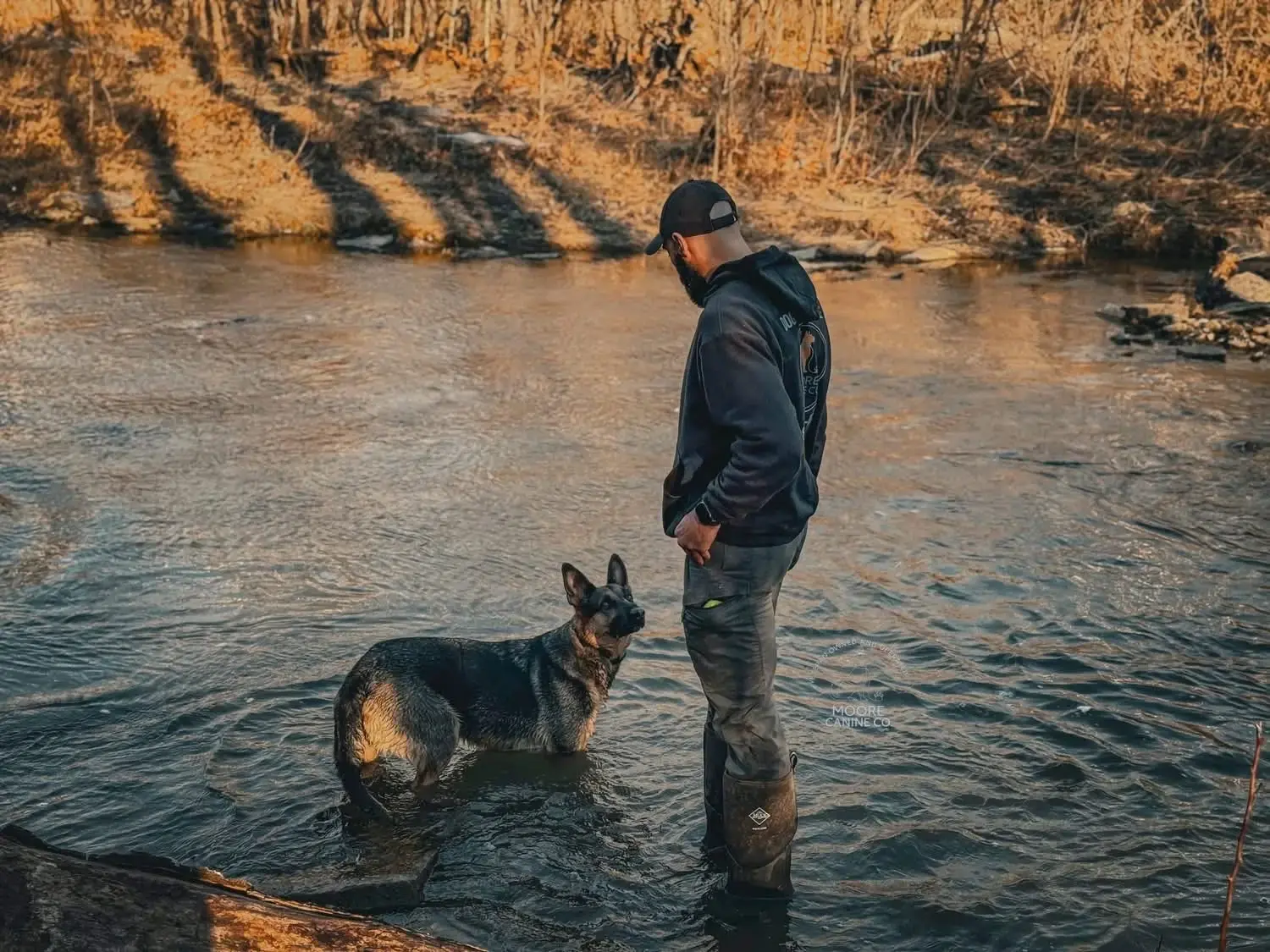 Nate and his German Shepherd sharing a quiet moment in a creek at golden hour