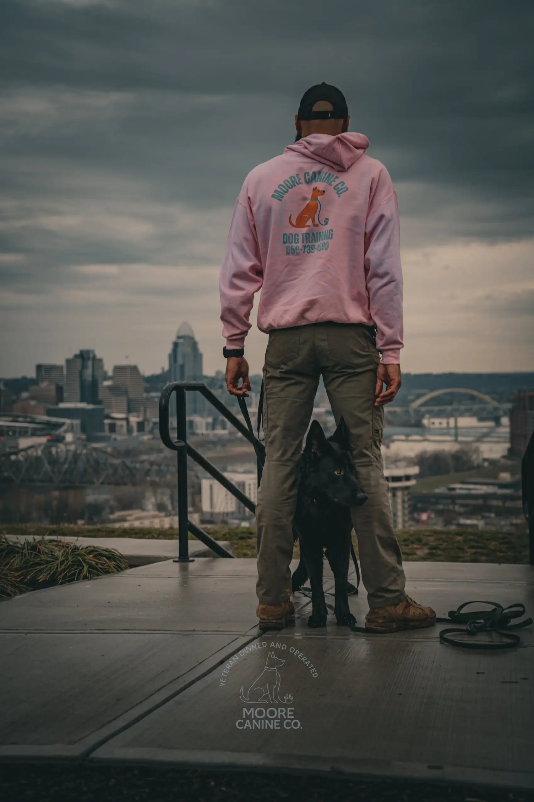 Nate Moore with a dog at heel, overlooking the Cincinnati skyline and the Ohio River bridges